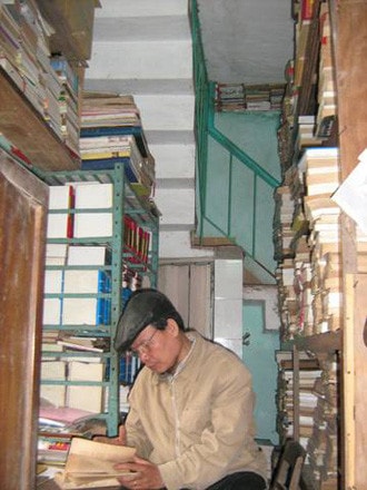 Ông Hùng ngồi đọc sách giữa kho sách đồ sộ trong nhà mình.
