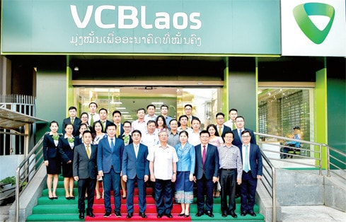 Ủy viên Bộ Chính trị, Thường trực Ban Bí thư Trần Quốc Vượng chụp ảnh lưu niệm với Đại diện Ban lãnh đạo Vietcombank, Ban Giám đốc và cán bộ nhân viên Vietcombank Lào trước Trụ sở Vietcombank Lào, tại Viên Chăn