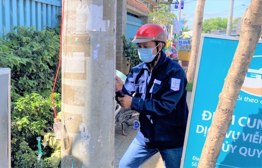 Công nhân Công ty Điện lực Hóc Môn đang xóa các chữ quảng cáo để làm sạch trụ điện