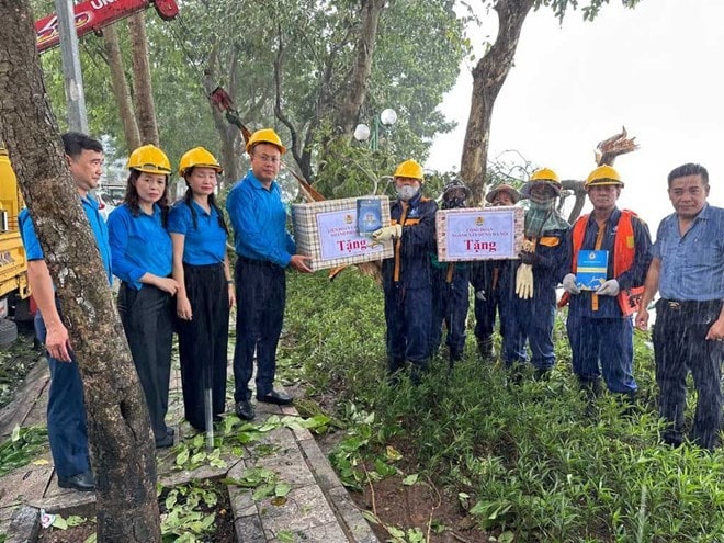 Chủ tịch Liên đoàn Lao động thành phố Phạm Quang Thanh và Chủ tịch Công đoàn ngành Xây dựng Hà Nội Nguyễn Thị Thanh tặng quà công nhân Công ty Trách nhiệm hữu hạn một thành viên Thoát nước Hà Nội đang dọn cây đổ bên bờ Hồ Tây. Ảnh: Việt Lâm