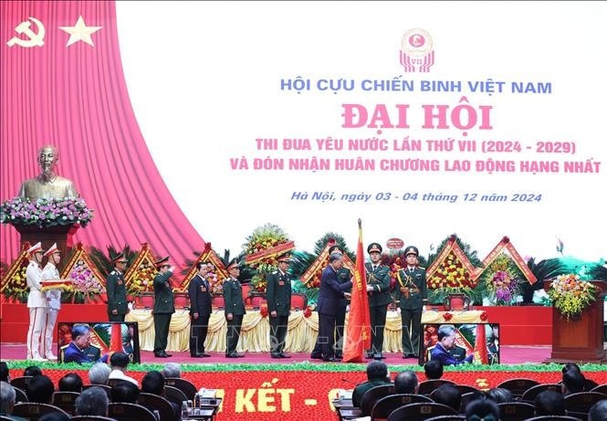 Tổng Bí thư Tô Lâm gắn Huân chương Lao động hạng Nhất lên lá cờ truyền thống Hội Cựu chiến binh Việt Nam. Ảnh: Thống Nhất/TTXVN
