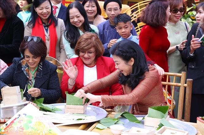 Bà Ngô Phương Ly, Phu nhân Tổng Bí thư Tô Lâm và các Đại sứ đã trải nghiệm gói bánh chưng. Ảnh: Văn Điệp/TTXVN