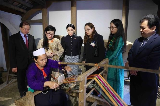 Bà Lê Thị Bích Trân, Phu nhân Thủ tướng Phạm Minh Chính và bà Loo Tze Lui, Phu nhân Thủ tướng Cộng hòa Singapore Lawrence Wong nghe Nghệ nhân giới thiệu về kỹ thuật dệt vải thổ cẩm. Ảnh: Phạm Kiên/TTXVN