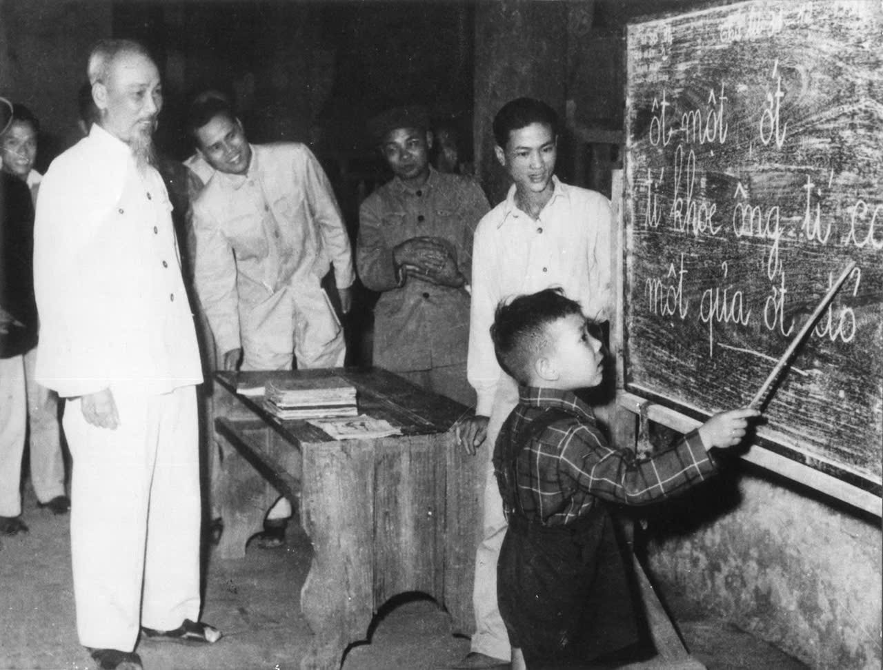 Bác Hồ quan sát một cháu thiếu nhi tập đánh vần khi đến thăm lớp học vỡ lòng Đình Thạch Khối ở phố Hàng Than, Hà Nội (31/12/1958). Ảnh: Bộ GD-ĐT