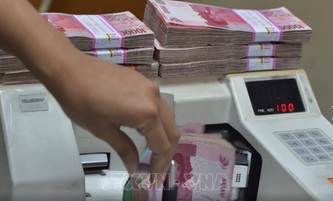 An employee at a foreign exchange office counts Indonesian rupiah banknotes. (Photo: AFP/VNA)