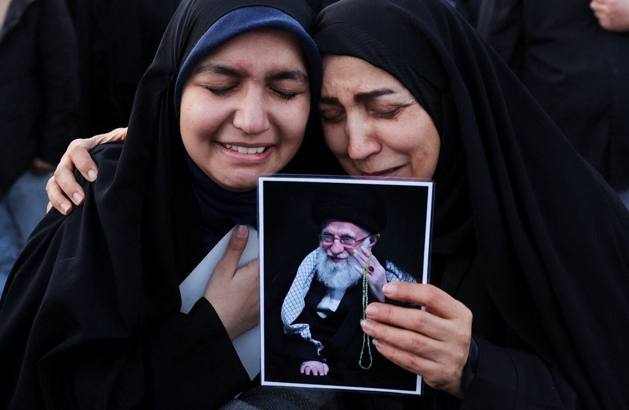 Two women in black cry as they hold an image.