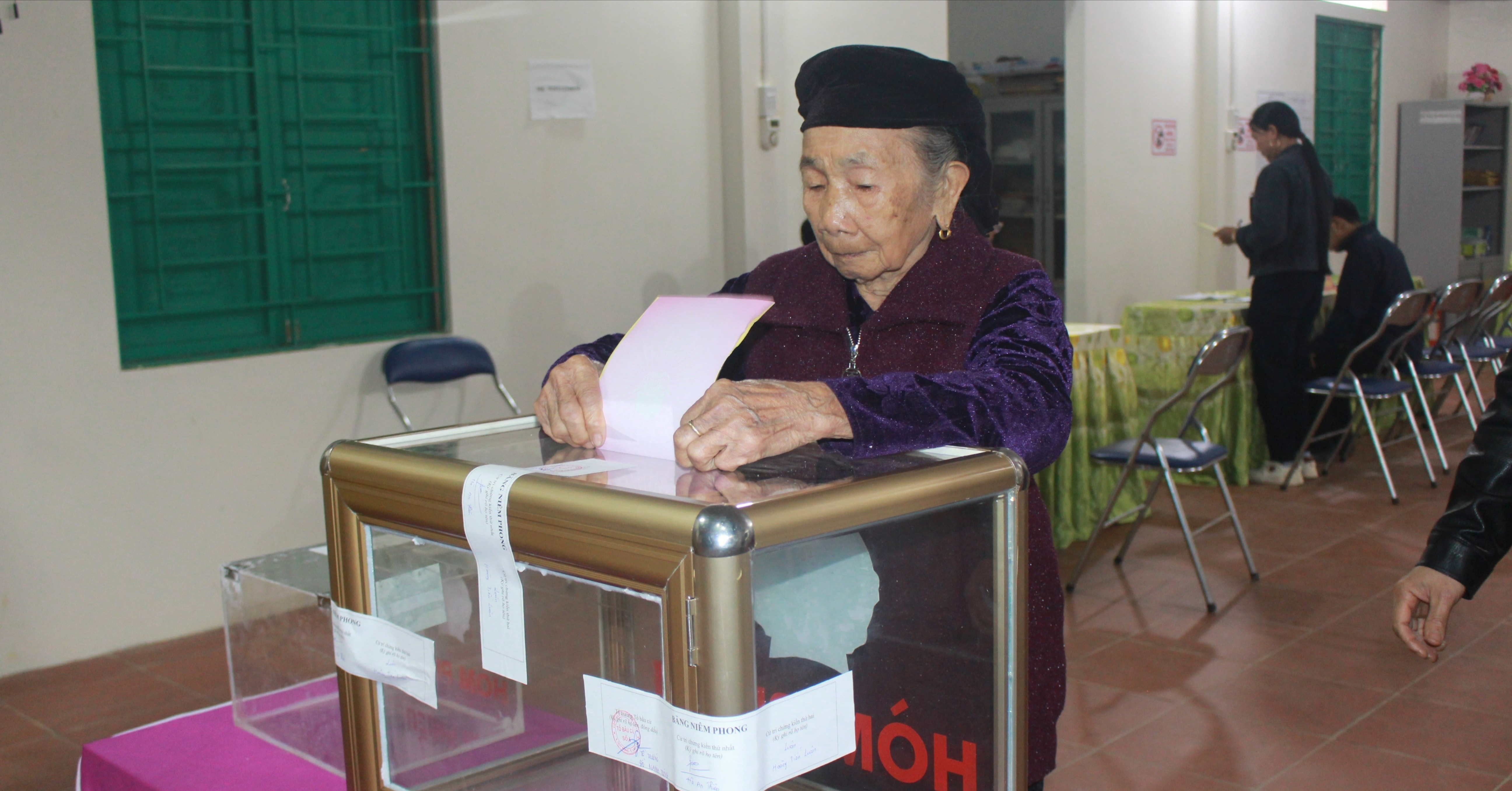 Mẹ Việt Nam Anh hùng Hà Thị Hao, thôn Kiên Lao, xã Quy Mông bỏ lá phiếu đầu tiên tại khu vực bỏ phiếu số 6 sau khi được người thân hỗ trợ tìm hiểu tiểu sử các ứng cử viên.