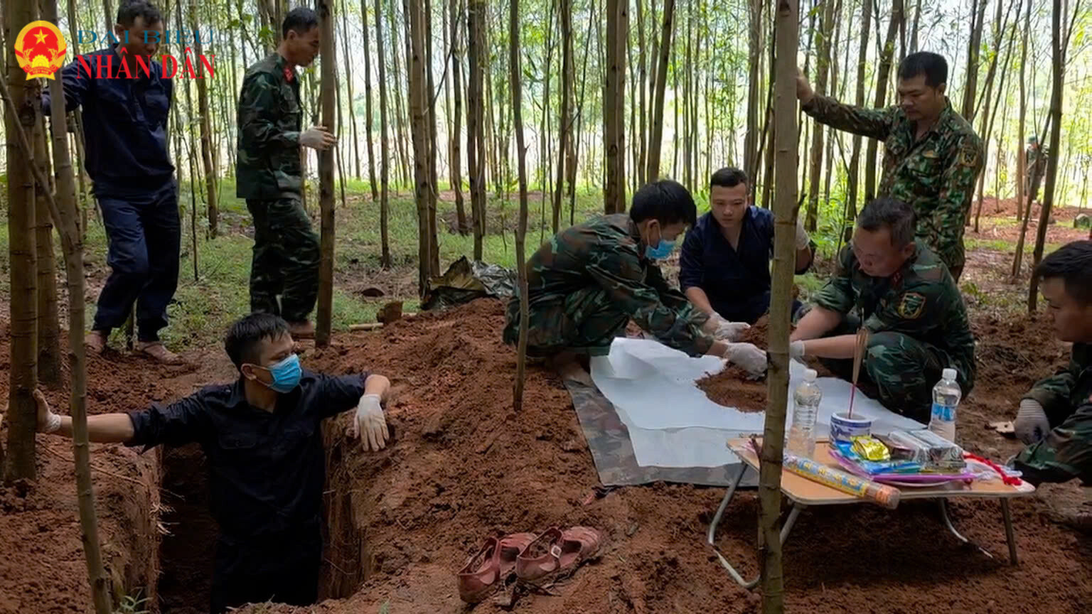 Đội tìm kiếm đang thực hiện cất bốc hài cốt liệt sĩ từ một hố mộ mới đào trong rừng tràm, tại Bãi Dinh bên cạnh có bàn thờ đặt hương, hoa và nước để thực hiện các nghi lễ tâm linh