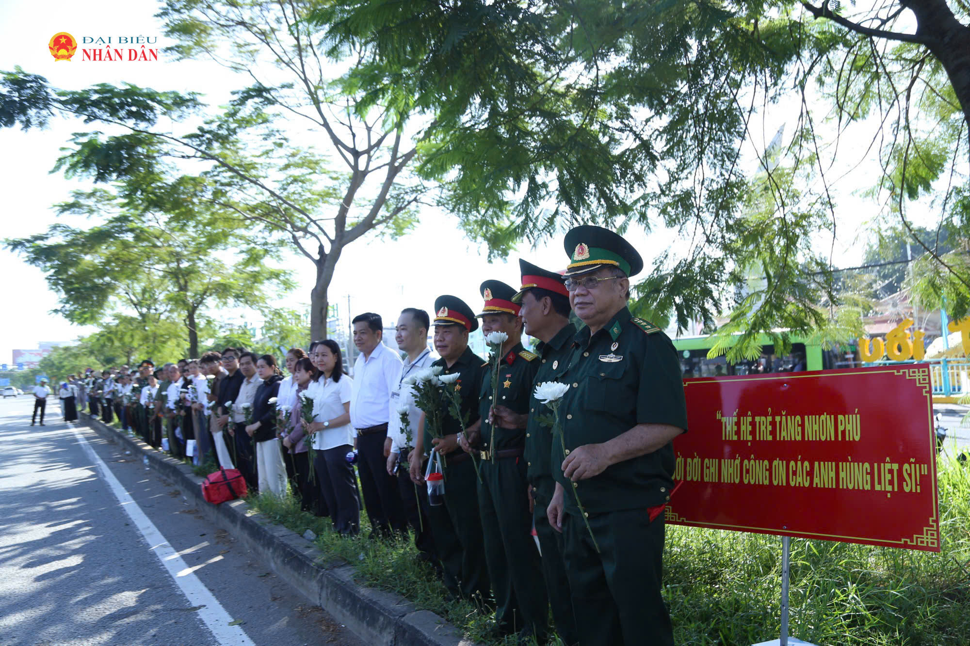 8h sáng, tại khu vực Khu du lịch Suối Tiên, đông đảo cựu chiến binh, người dân phường Tăng Nhơn Phú mang theo hoa cúc trắng, đứng thành hàng dọc bên đường Xa lộ Hà Nội chờ đưa tiễn các Anh hùng liệt sĩ